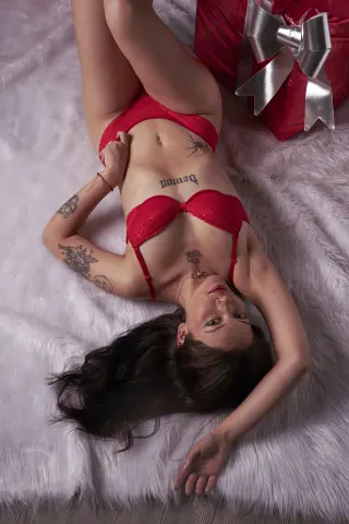 Tattooed woman in red lace lingerie lying on a white faux fur rug for a romantic Valentine's Day mood.