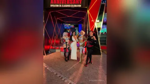 NohomiCambel stands in a white dress with three other performers in front of a black and red anniversary stage set.