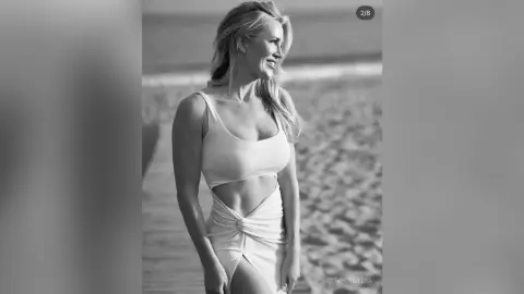 Smiling blonde woman in a white cutout bodysuit relaxing on a sunny beach in a black and white portrait.