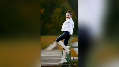 Stylish woman in white puffer jacket and black leggings posing on a wooden pier during a golden autumn sunset.