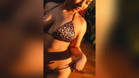 Young woman in a leopard print bikini relaxing in warm, golden sunlight for a summer vacation mood.