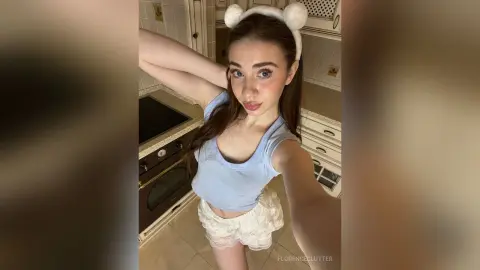 Young woman in a light blue crop top and white lace shorts wearing a cute bear headband in a bright kitchen.
