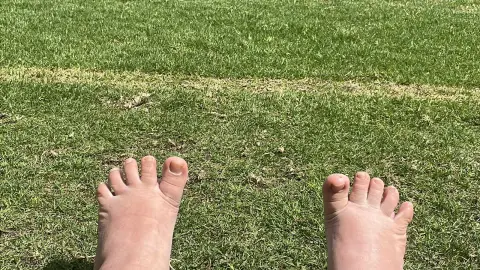Bare feet resting on lush green grass in a peaceful outdoor park setting.