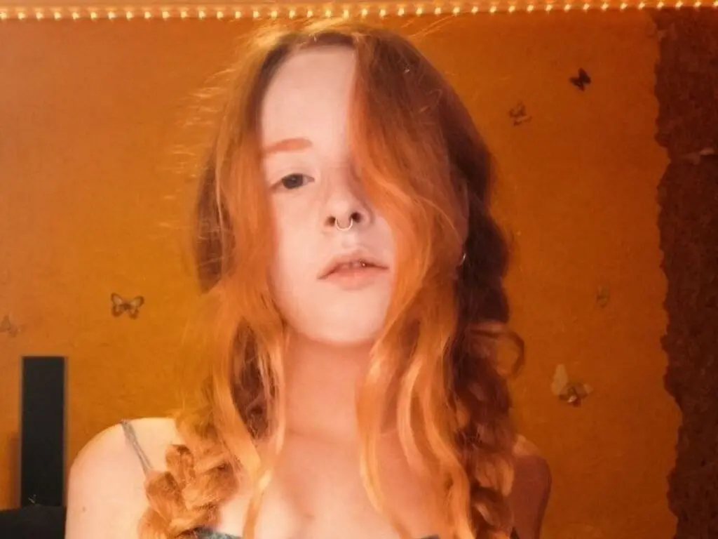 Redheaded woman in a casual strap top posing in warm, glowing light with a dreamy mood.