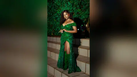 Elegant woman in a sparkling emerald green evening gown posing on outdoor stairs at night.