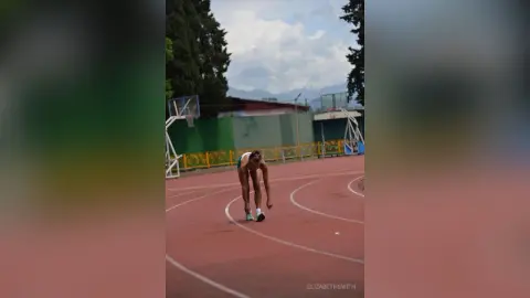 Athletic woman in blue workout gear training on a red outdoor running track under a cloudy sky.