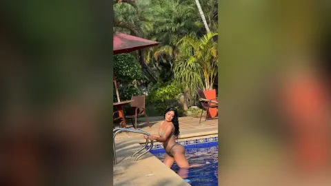 Young woman in a green bikini relaxing by a tropical resort swimming pool on a sunny day.