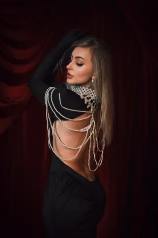 Elegant woman in a black backless dress with pearl embellishments posing against a red velvet curtain.