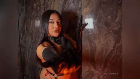 Moody portrait of a woman in a black choker and gloves against a dark marble wall background.