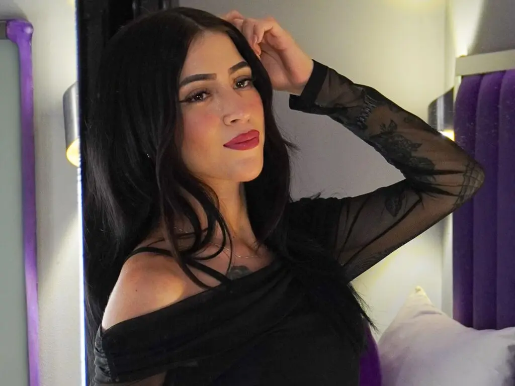LilyTarazona poses with her hand in her long black hair, wearing a black sheer long-sleeve top.