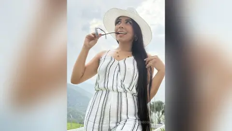 Smiling woman in a white striped romper and sun hat enjoying a sunny summer day outdoors.