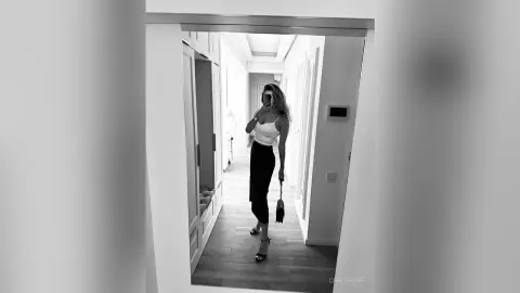 Stylish woman in a white tank top and black trousers standing in a bright modern hallway, black and white aesthetic.