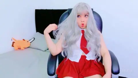 HimeJess wearing a white vest and red skirt, posing with her long silver hair while sitting in a black chair.