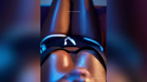 Close-up of a woman in black lingerie relaxing in moody, cinematic blue and warm lighting.