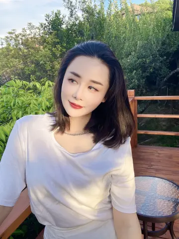 Elegant woman in a white t-shirt relaxing on a wooden deck surrounded by lush green garden foliage.