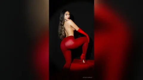 Glamorous woman in red leggings and gloves posing against a dark background with dramatic red lighting.