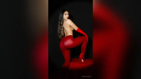 RosieThomas — Glamorous woman in red leggings and gloves posing against a dark background with dramatic red lighting.