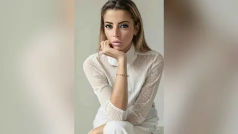 Elegant woman in a white sheer blouse posing with a serene expression against a neutral studio background.