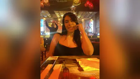 Smiling woman in a black tank top enjoying a cozy evening at a dimly lit restaurant.