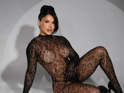Glamorous woman in a black sheer leopard print bodysuit posing against a grey studio background.