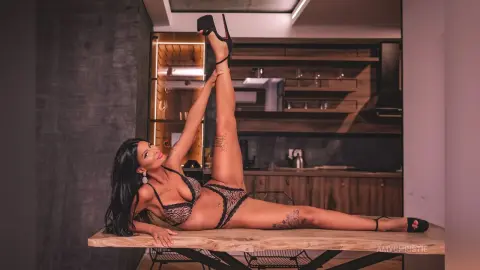 Fit woman in patterned bikini lounging on a wooden table in a modern kitchen setting.