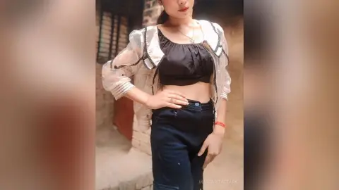 Young woman in a black crop top and dark jeans posing confidently in a rustic outdoor setting.