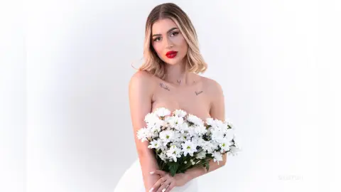 DaisyLin poses against a white background, holding a large bouquet of white daisies against her bare chest.