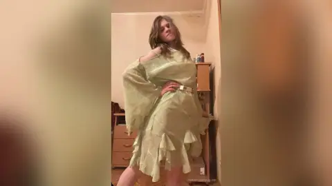 Woman in a sage green ruffled maxi dress posing in a cozy indoor setting.