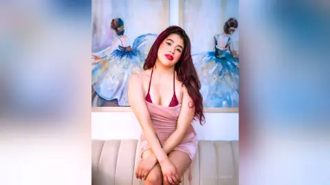 Beautiful woman in a pink slip dress sitting before ballet paintings in a bright, elegant room.