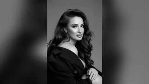 AnnaKarev poses with long wavy hair and a black blazer looking at the camera in this black and white portrait.