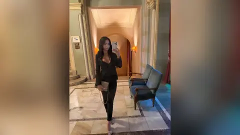 Stylish woman in a black blazer and trousers taking a mirror selfie in a luxury marble hallway.
