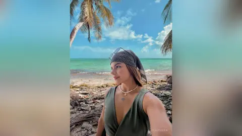 Smiling woman in a green tank top and bandana relaxing on a sunny tropical beach with palm trees.