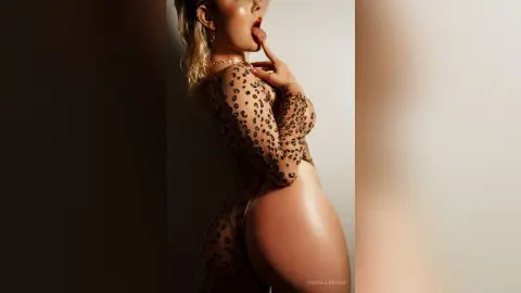 FiorellaRossi poses in a long-sleeved leopard print bodysuit, sucking on her finger with her head tilted back.