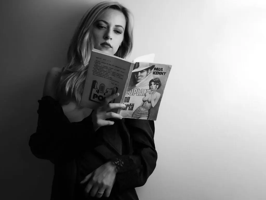 Moody black and white portrait of a young woman reading a Paul Kenny book in a minimalist setting.