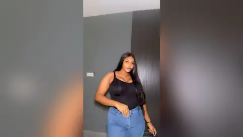 Young woman in a black bodysuit and blue jeans posing confidently in a modern minimalist room.