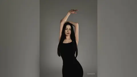 Elegant woman in a sleek black dress posing gracefully against a minimalist grey studio background.