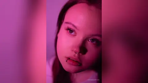 Young woman with nose ring and moody pink lighting in a cinematic close-up portrait.