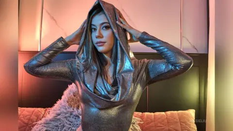 JessieLiu wears a silver metallic hooded bodysuit while posing with her hands against her head.