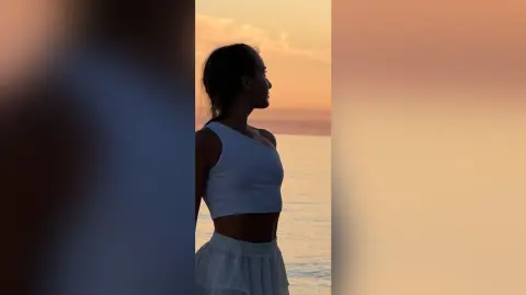 Silhouette of a woman in a white crop top enjoying a peaceful sunset over the ocean.