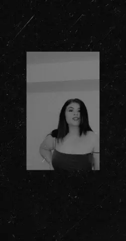 Moody black and white portrait of a young woman in a dark camisole top against a minimalist background.
