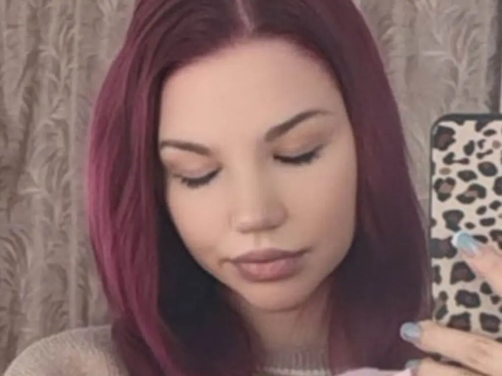 Young woman with dyed magenta hair taking a soft, moody selfie in a cozy indoor setting.