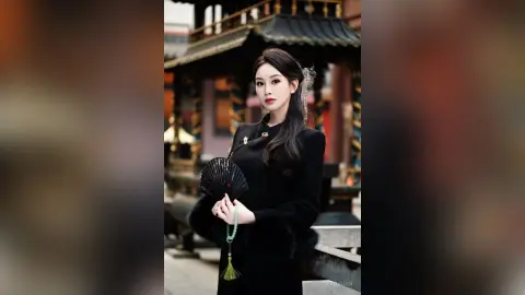 Elegant woman in a black traditional Hanfu holding a folding fan in a historic Chinese temple courtyard.