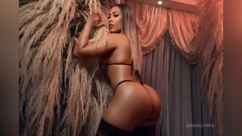 Curvy woman in black lingerie posing amidst soft pampas grass decor in a dreamy, romantic setting.