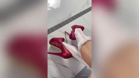 Woman in white lace socks and sparkly pink high heels walking on a marble floor.