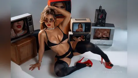 Glamorous woman in black bikini and sunglasses posing amidst vintage televisions in a retro studio setting.