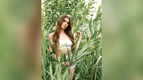 Young woman in a white crop top posing in a lush green field during a serene summer sunset.