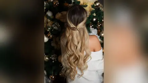 DenisePerry poses with her back to the camera, showing her long blonde wavy hair styled with a gold leaf clip in front of a Christmas tree.