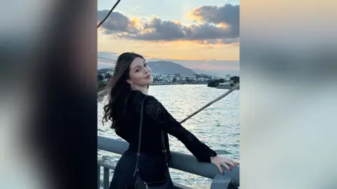 Smiling woman in a black long-sleeve top enjoying a sunset boat ride on the ocean.