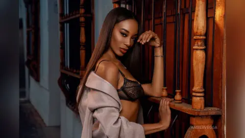 Elegant woman in a lace bra and beige cardigan posing by a vintage wooden balcony at sunset.