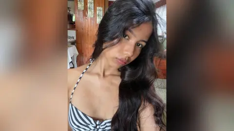 Young woman with long wavy hair wearing a black and white striped bikini top in a cozy indoor setting.